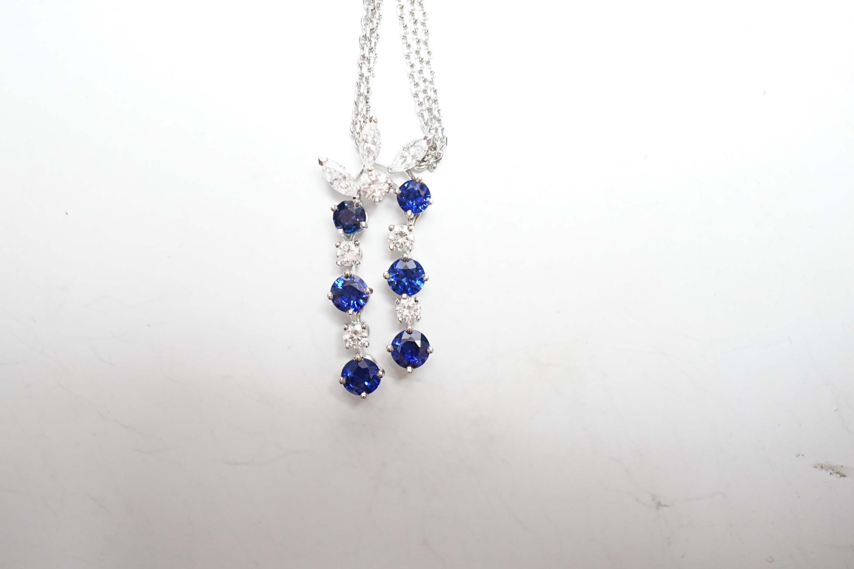 A modern 750 white metal, sapphire and diamond set cluster pendant, 31mm, on a twin strand white metal chain, 44cm, gross weight 10.3 grams, in a Bucherer box.